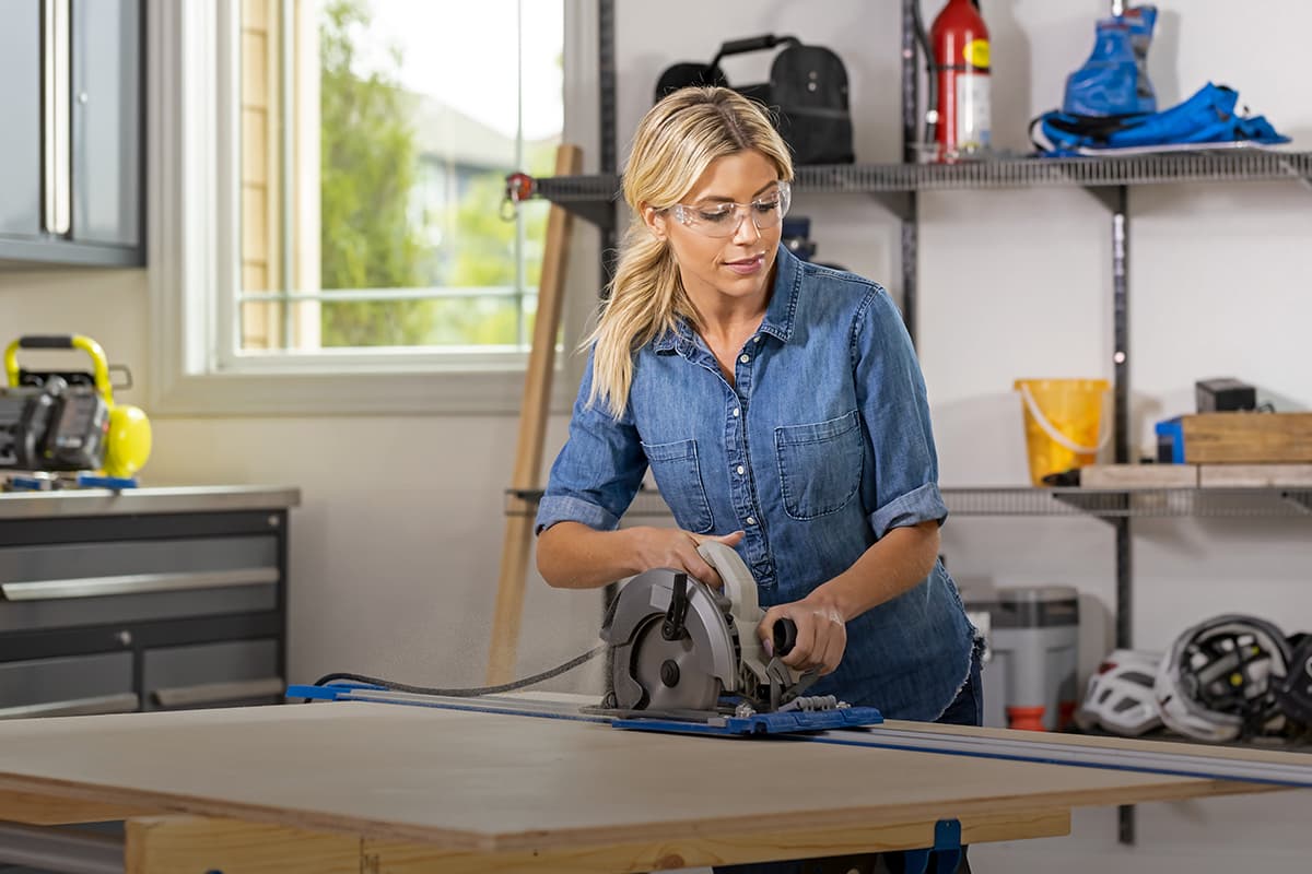 Image of a woman cutting a piece of plywood with a circular saw and guide